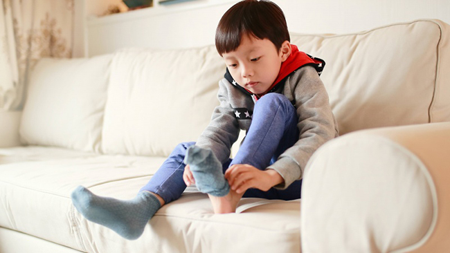 child sitting on a sofa, putting on a sock