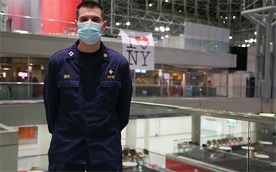 a masked Dr. Smith in large hall with I heart NY banner in background