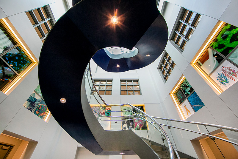 Spiral Staircase rising through the middle of the building with artwork along the walls.