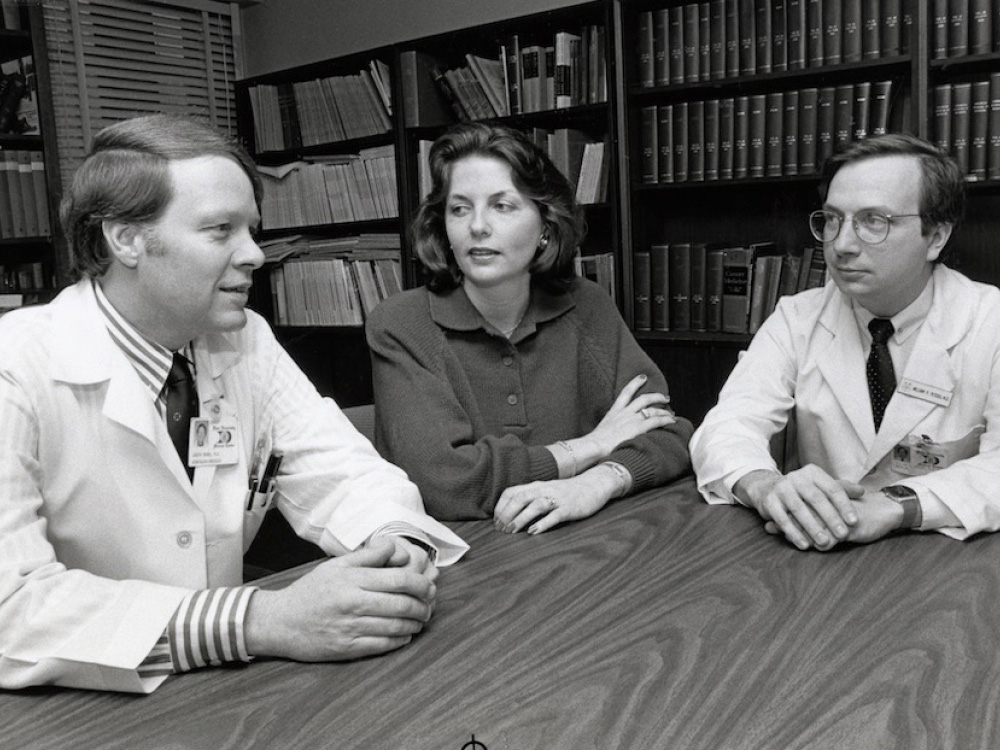 black and white photo of two men and one woman sitting at table talking