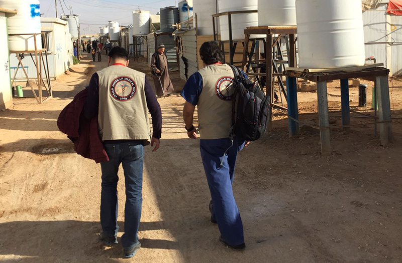 Dr. Akhter and a colleague walking through a refugee camp wearing SAMA vests