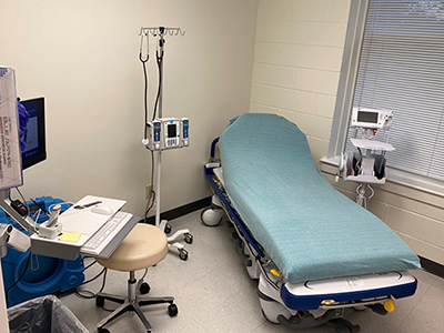 image of Pickett Road exam room. A patient bed with a blue sheet, an IV pole, a computer.
