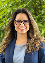 Student Alissa Arango smiling at camera wearing glasses, blue shirt and blue blazer in front of trees with curled hair over both shoulders