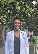 Student Santita Ebangwese in white coat standing in front of tree