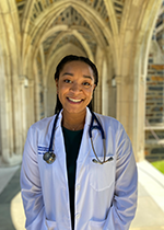Student Amika Ekanem in white coat and stethoscope standing under archway