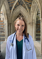 Student Megan Happ wearing white coat and stethoscope standing under archway