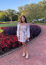 Student Jamie Karl wearing floral long sleeve dress standing in front of flower bed