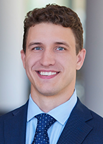 Headshot of student John Leschisin wearing blue suit with blue tie