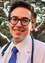 Headshot of student Nathan Luzum wearing white coat & Stethoscope in front of a tree