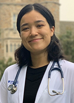 Student Ellen Mines wearing white coat and stethoscope in front of brick building