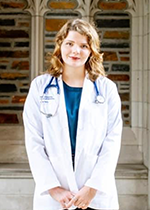 Student Raquel Perry wearing white coat and stethoscope standing in front of brick wall