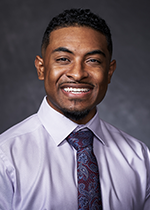 Headshot of student Reef Shah in front of grey background wearing lilac shirt and purple printed tie
