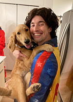 Student Kyle Steinbock smiling at camera holding golden medium-sized dog