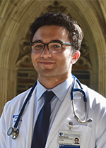 Student David Sykes wearing white coat and stethoscope in front of brick wall