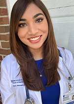 Student Ivana Premasinghe smiling at camera wearing white coat and stethoscope over blue dress