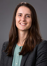 Headshot fo MSTP student Eleanor Semmes wearing black blazer over green shirt with brown hair over shoulders in front of grey background