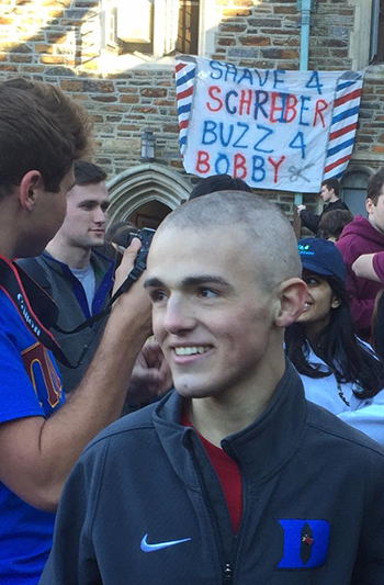 Bobby Menges with a shaved head. Sign reads shave a schreiber buzz 4 Bobby
