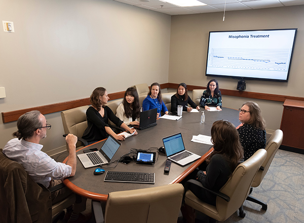 Dr. Rosenthal and other researchers meeting around an oval table with a large presentation screen in the background