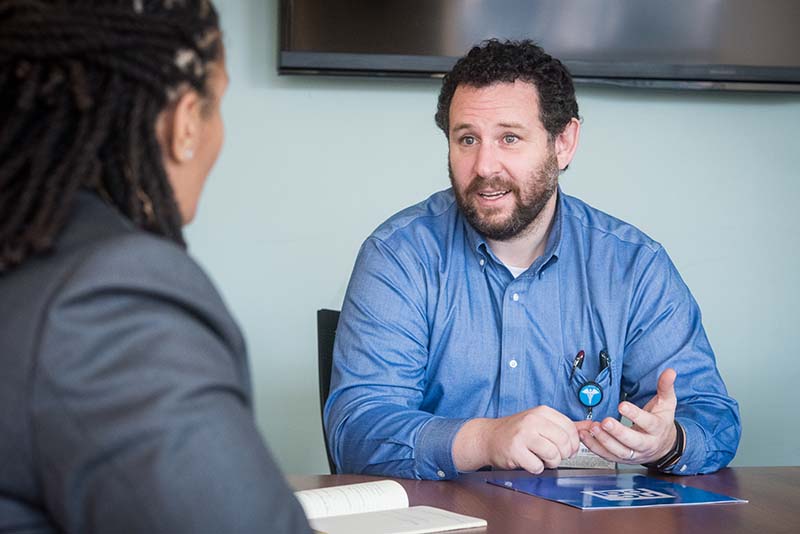 man seated at table speaking to another person