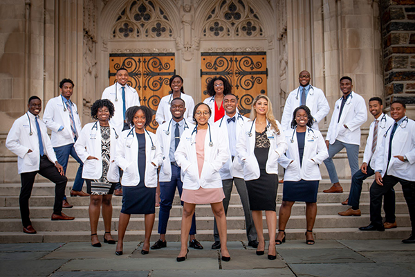 Group of Black and Brown medical students in white coats on the steps of Duke Chapel