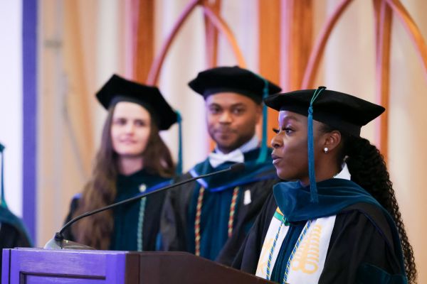 A graduate speaking at the podium with two peers in background