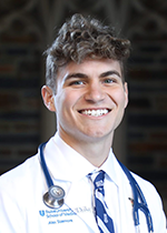 Alex Sizemore headshot smiling at camera, short curly hair wearing white coat and stethoscope in front of slightly blurred brick wall backdrop