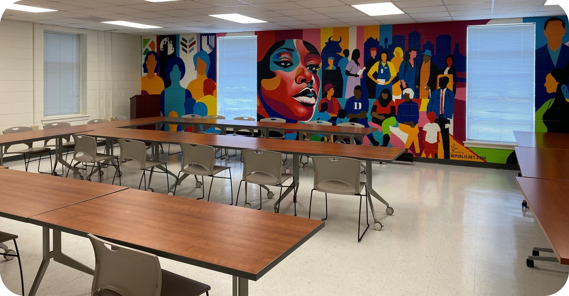 Image of a room with long tables, chairs and a mural along the farthest wall.