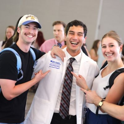 Three students pointed at a male student who just received his white coat 