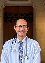 Student smiling at camera wearing glasses, white coat, stethoscope and floral tie