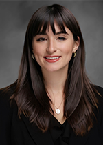 Headshot of Kayla Corredera-Wells smiling at camera with long brown straight hair and bangs falling in front of shoulders over black shirt