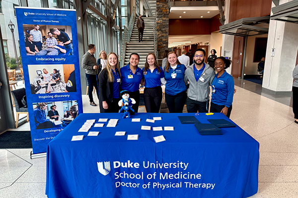 students posing for a photo behind the open house welcome table