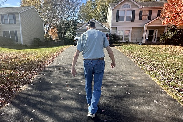 photo of a man from behind, walking up the driveway toward his house