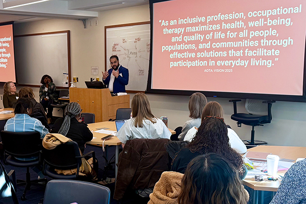 Warren talking to an audience of prospective Duke OTD students with an AOTA message about inclusion displayed on the screen