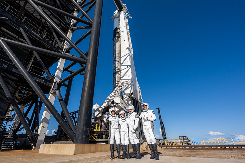 Three astronauts standing in front of a rocket ready to launch