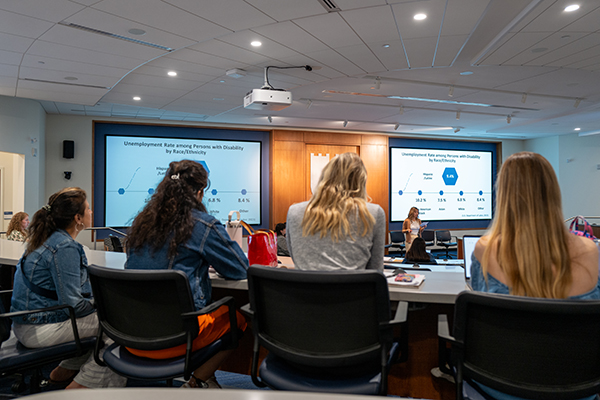 students in the foreground facing a student speaking at the front of the classroom in the background