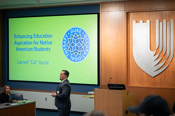 a student presenting in front of a lecture hall projection screen