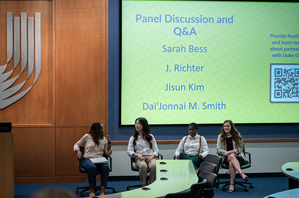 four students at the front of a lecture hall for a panel