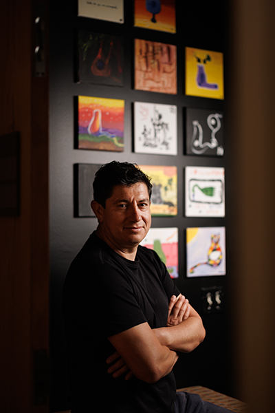 Diego Bohórquez, PhD, sitting on a bench in his lab in front of artwork on the wall