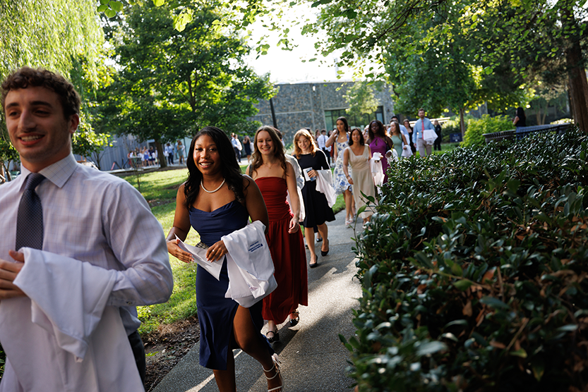 Students walking into the white coat ceremony with their coats folded over their arms