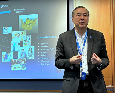 Michael Iwama speaking in front of a slide presentation