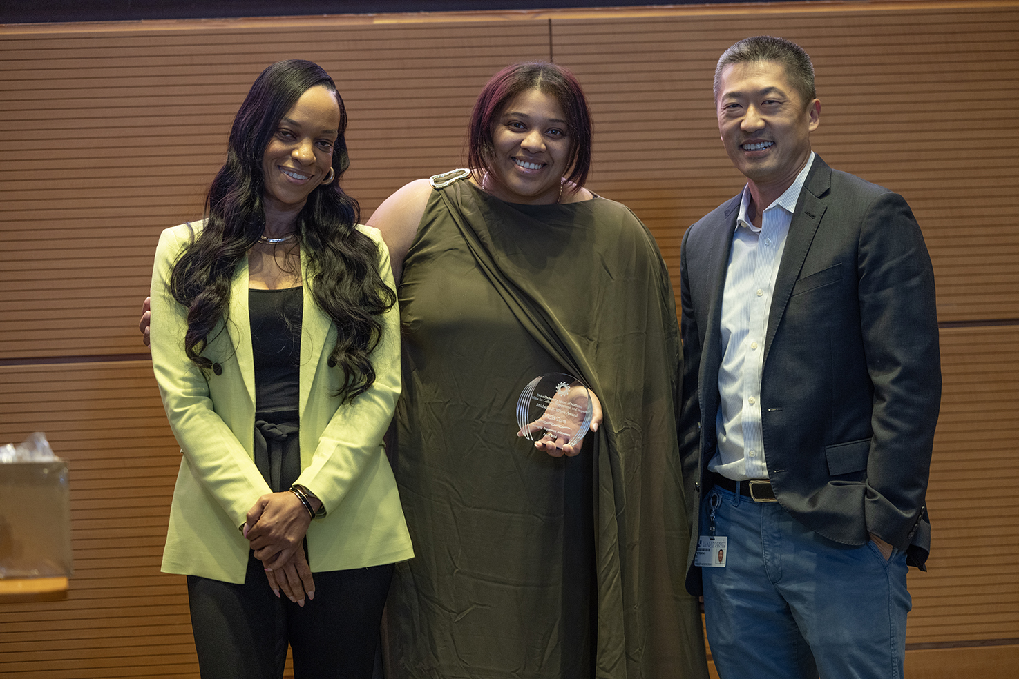 Three people smiling holding an award