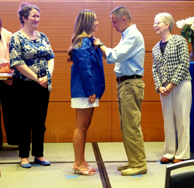 Female OTD student stands on stage to get a pin from her dad