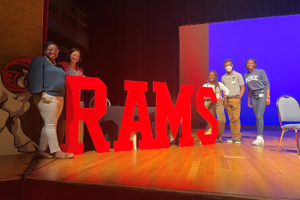 Kendra with others next to a large "RAMS" sign