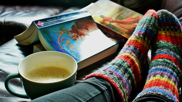 A person with a book and a cup of coffee. The person is wearing fuzzy colorful socks.