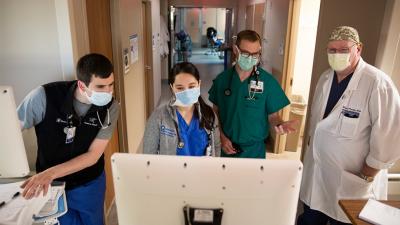 two medical students look at computer screen with two providers in hospital