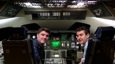 Two students sitting in the cockpit of a model of the space shuttle