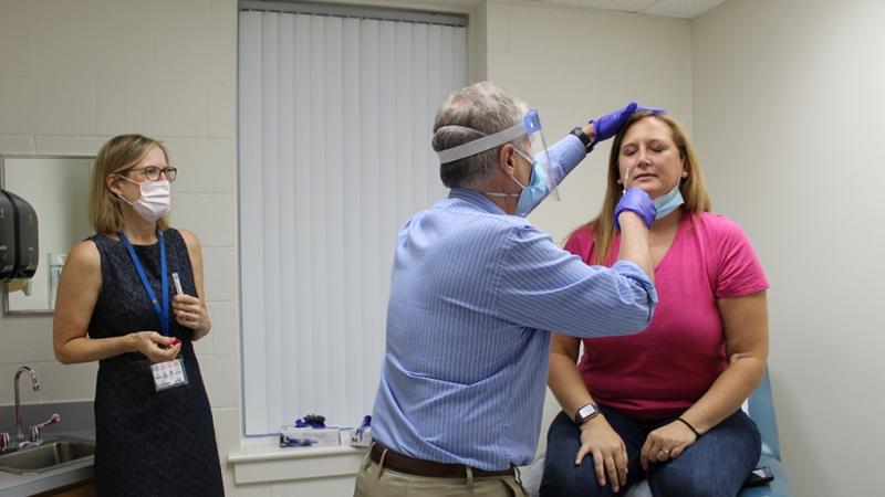 patient getting her nose swabbed for a COVID test, researcher standing by.