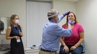 patient getting her nose swabbed for a COVID test, researcher standing by.