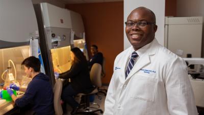 Dr. Olabisi in his lab, people working under safety hoods behind him.