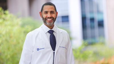 Black male physician in white coat standing outside